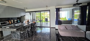 A modern kitchen with a central island, bar stools, and a dining area with a view of the outdoors.