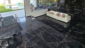 Un interior moderno con piso de mármol negro, sofá blanco con cojines estampados y una puerta de vidrio que da a un espacio exterior.