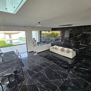 A modern interior with a black marble floor, a white sofa with patterned cushions, and a glass door leading to an outdoor area.