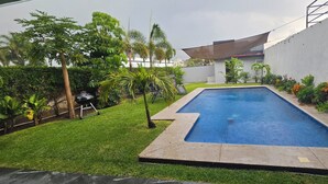 A rectangular swimming pool with a surrounding grassy area and various plants.