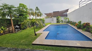 A rectangular swimming pool with a surrounding grassy area and various plants.