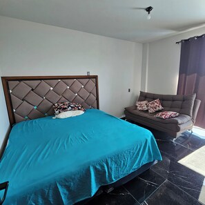 A bedroom with a bed, a sofa, and a ceiling fan.