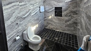 A bathroom with a marble wall, a toilet, a towel rack, and a shower area.
