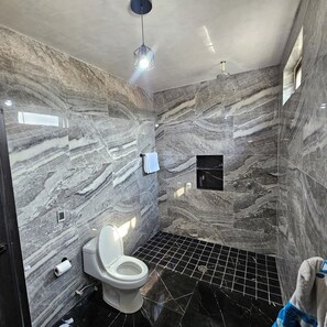 A bathroom with a marble wall, a toilet, a towel rack, and a shower area.