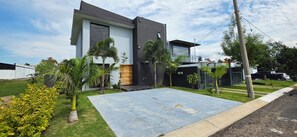 A modern two-story house with a flat roof, a large patio area, and a well-maintained lawn.