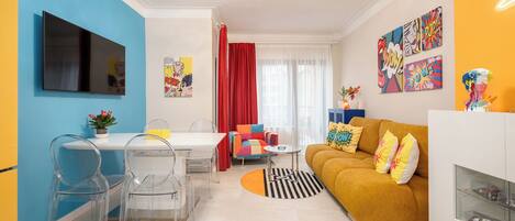 A modern living room with a sofa, a dining table with chairs, and a TV mounted on the wall.