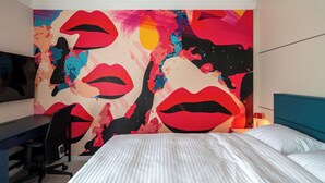A bedroom with a large abstract wall art, a bed with white linens, a desk with a chair, and a blue headboard. - Pop-Art Apartment Sofia I 9 people I 3 Bedrooms I 3 Bathrooms I Design awarded (Sofia)