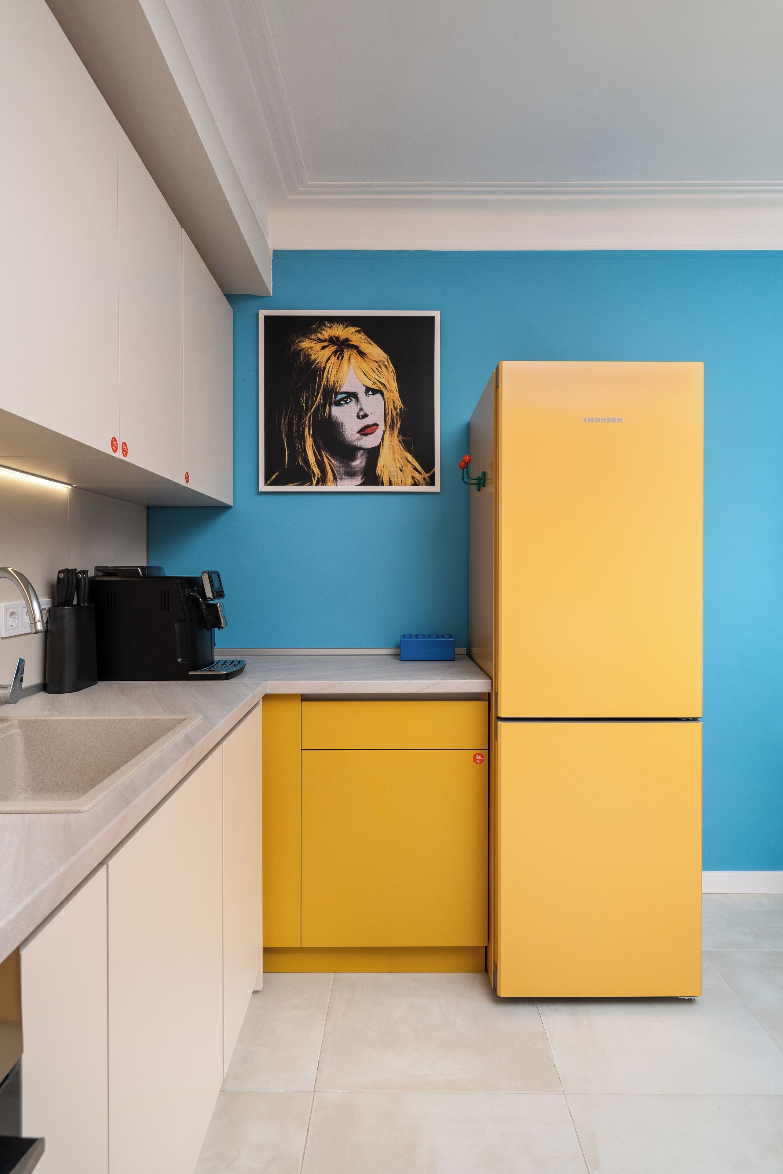 A kitchen with a yellow refrigerator, a blue wall, and a framed picture above the counter.