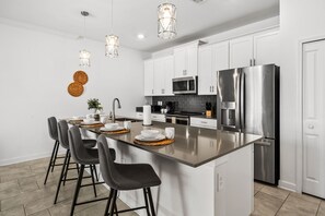 Uma cozinha moderna com uma ilha central, eletrodomésticos de aço inoxidável e iluminação pendente.
