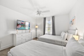 Ein Hotelzimmer mit zwei Betten, einem Deckenventilator, einem Fernseher, einem Schreibtisch und einem Fenster mit Vorhängen.
