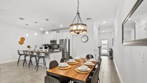 A modern kitchen with white cabinets, stainless steel appliances, and a dining area with a wooden table set for six. - Sleeps 10 *Private Pool *FREE Waterpark Access! (Kissimmee)