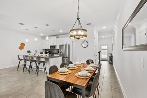 Cozinha moderna com armários brancos, eletrodomésticos de aço inoxidável e área de jantar com mesa de madeira para seis pessoas.