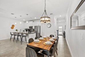 Une cuisine moderne équipée d’appareils électroménagers en acier inoxydable, un coin repas avec une table et des chaises en bois, et un grand miroir au mur.