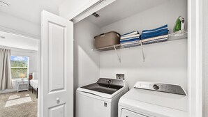 A laundry room with a front-loading washer and dryer, a shelf with folded towels, and a basket. - Sleeps 10 *Private Pool *FREE Waterpark Access! (Kissimmee)