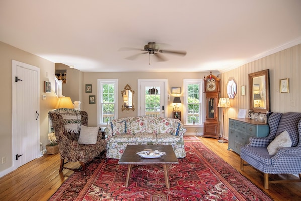 A living room with a sofa, armchairs, a coffee table, a clock, and a ceiling fan.