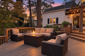 An outdoor deck with wicker furniture, a fire feature, and a house in the background.