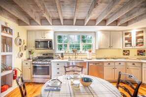 A kitchen with wooden beams, white cabinets, a stove, a microwave, and a window with a view of greenery.