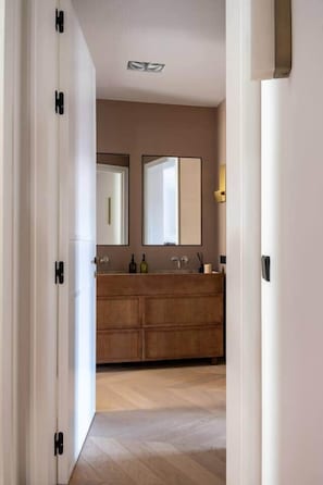 A hallway leading to a bathroom with a wooden vanity, two mirrors, and a light fixture. - Príncipe Executive Residence (Madrid)
