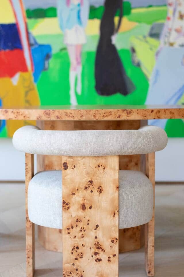 A wooden stool with cushioned seats and a painting in the background.