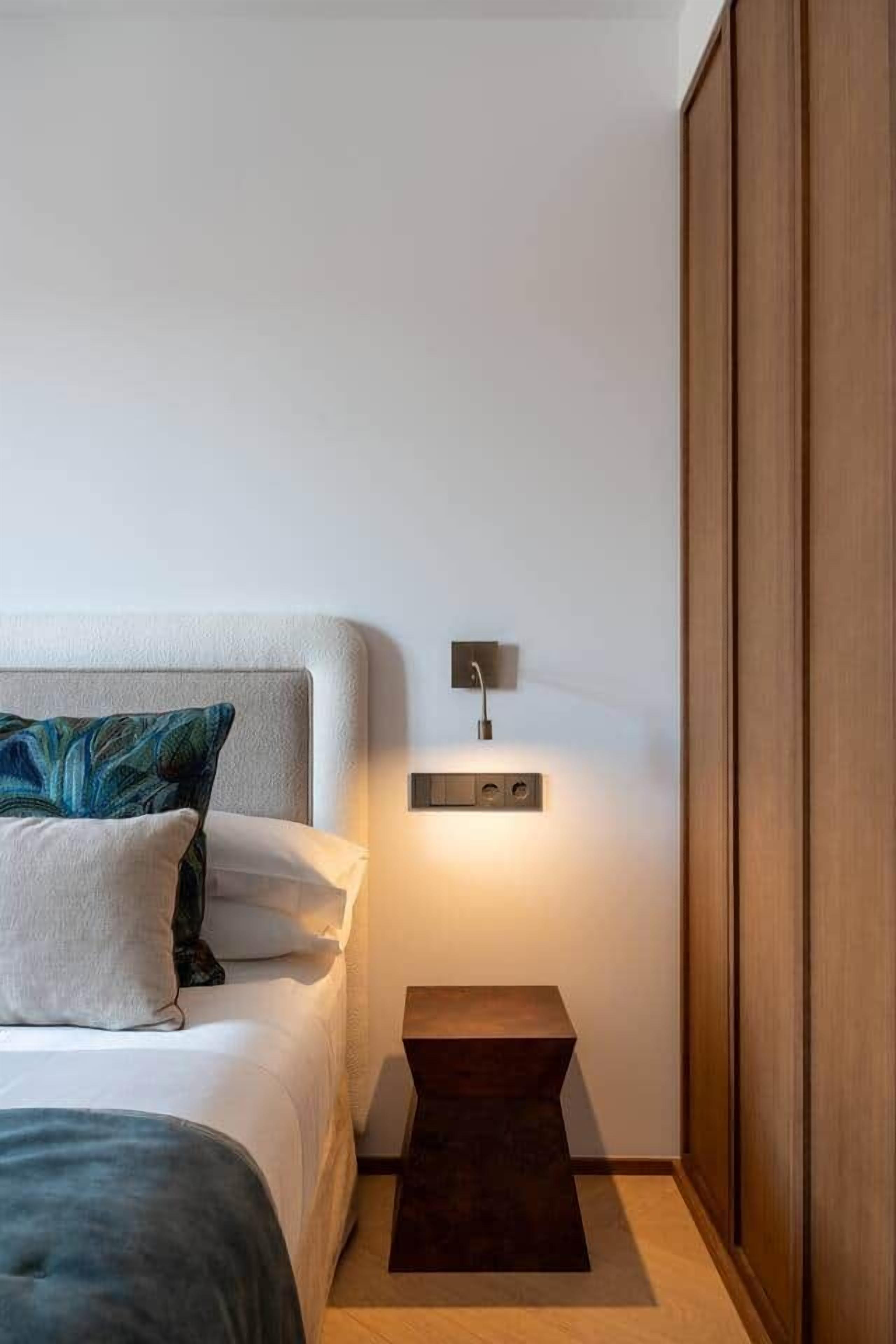 Een slaapkamer met een bed, nachtkastje en een wandlamp.