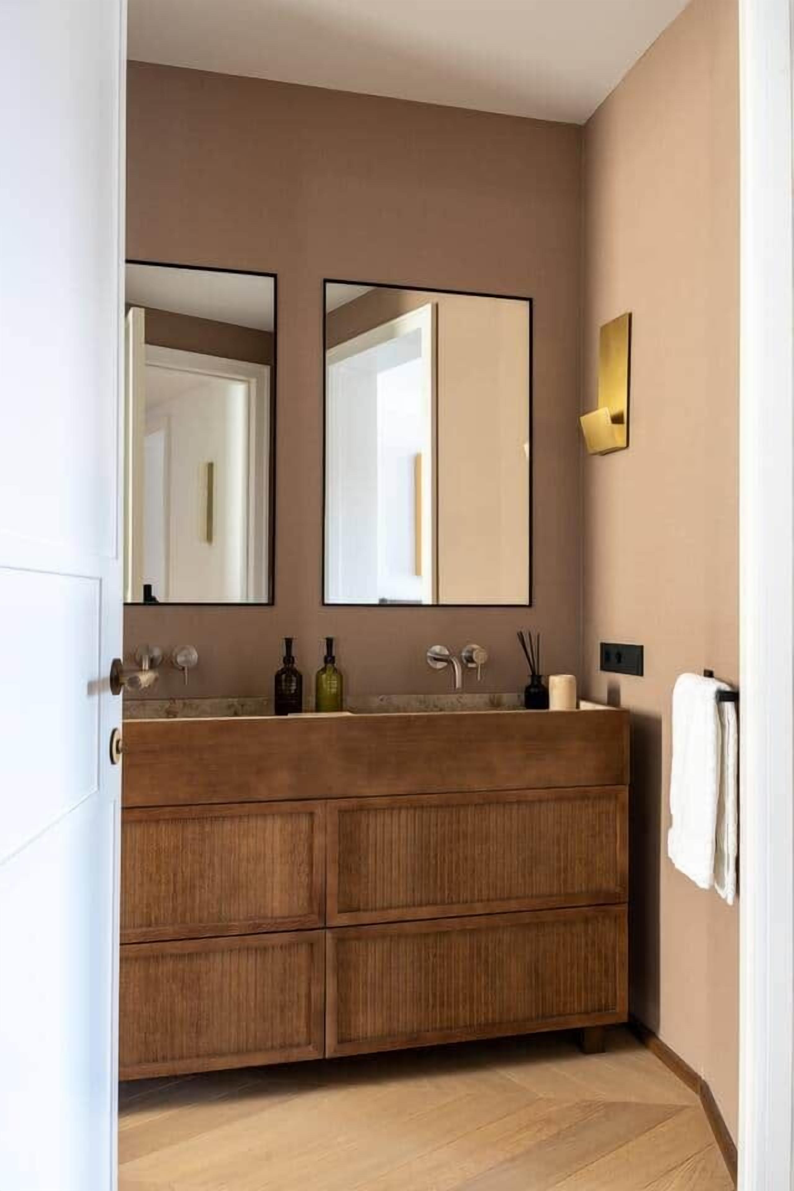 Un baño moderno con tocador de madera, dos espejos y un aplique en la pared.