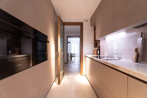 A modern kitchen with integrated appliances, a central island, and a view into the dining area. - Príncipe Executive Residence (Madrid)