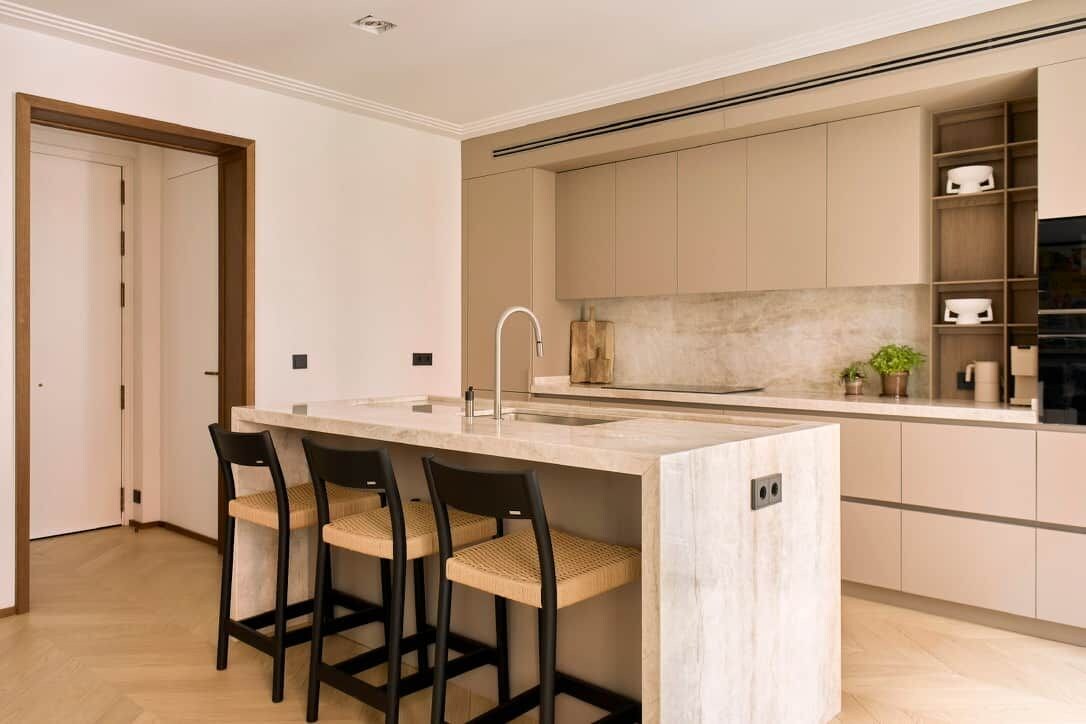 Una cocina moderna con una isla central, taburetes de bar y armarios empotrados.