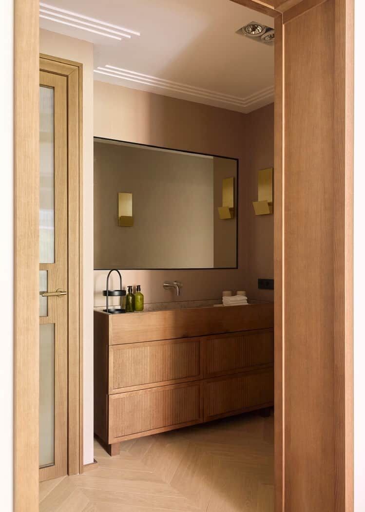 A modern bathroom with a large mirror, wooden vanity, and a light fixture on the ceiling.