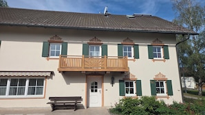A two-story building with a balcony, a bench, and a small garden area. - Lovingly renovated farmhouse for 2–6 adults (+ 2 children) in a quiet location (Reisbach)