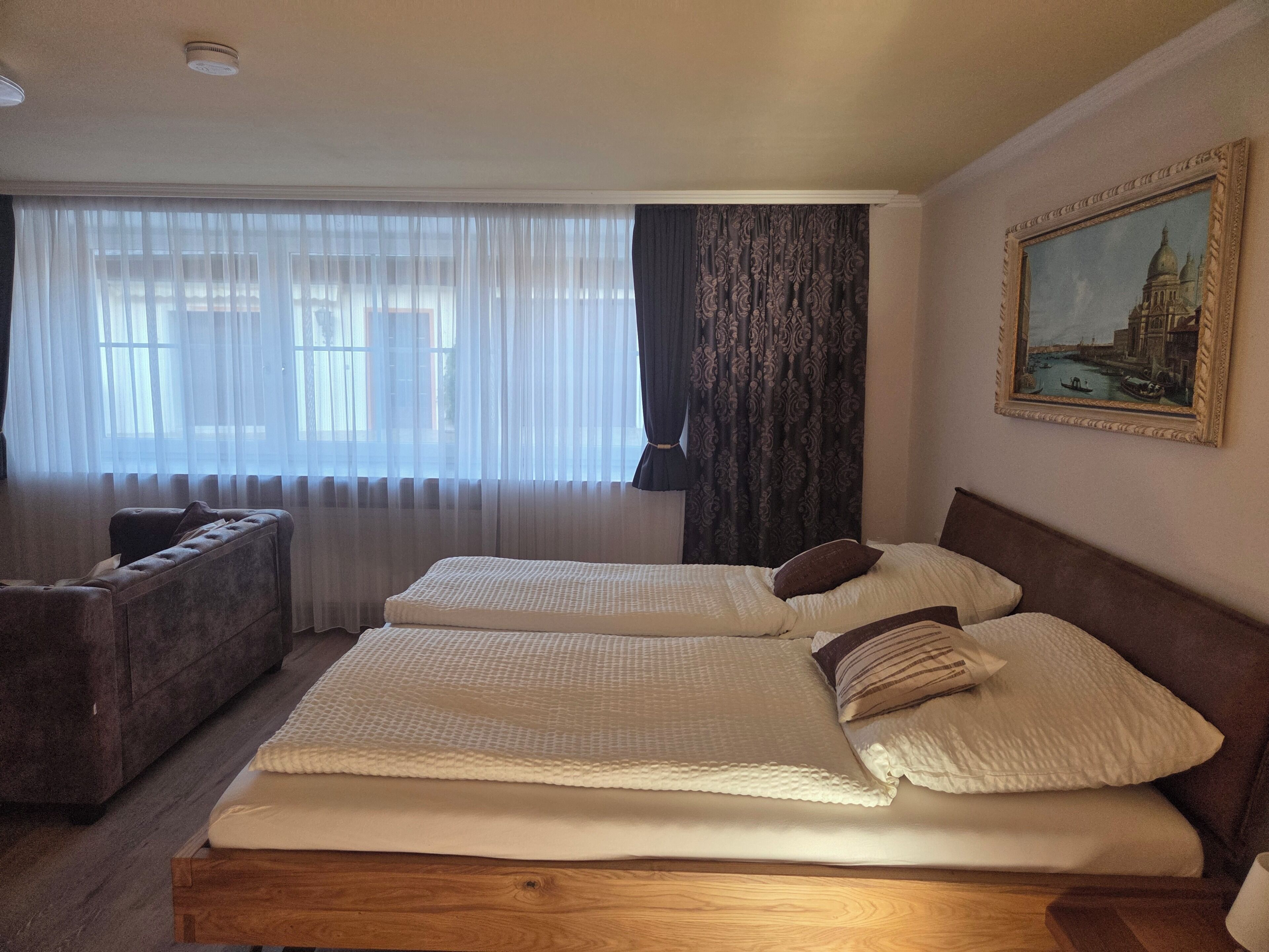 A hotel room with two beds, a sofa, and a large window with sheer curtains.
