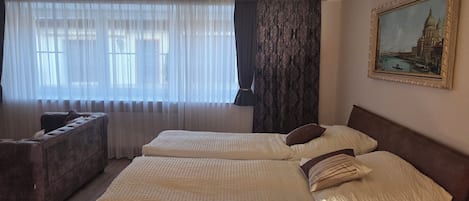 A hotel room with two beds, a sofa, and a large window with sheer curtains.