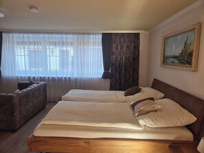 Ein Hotelzimmer mit zwei Betten, einer Sitzecke und einem großen Fenster mit durchsichtigen Vorhängen.