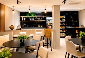 A modern interior with round tables, chairs, and a bar area with shelves stocked with snacks and beverages. - Breeze Residence 509 Beachfront Apartment on Bessa   (João Pessoa)