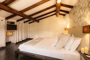 Ein Schlafzimmer mit Holzbalkendecke, einem Bett mit weißer Bettwäsche, einem Nachttisch mit Kerzen und einem an der Wand befestigten Fernseher.