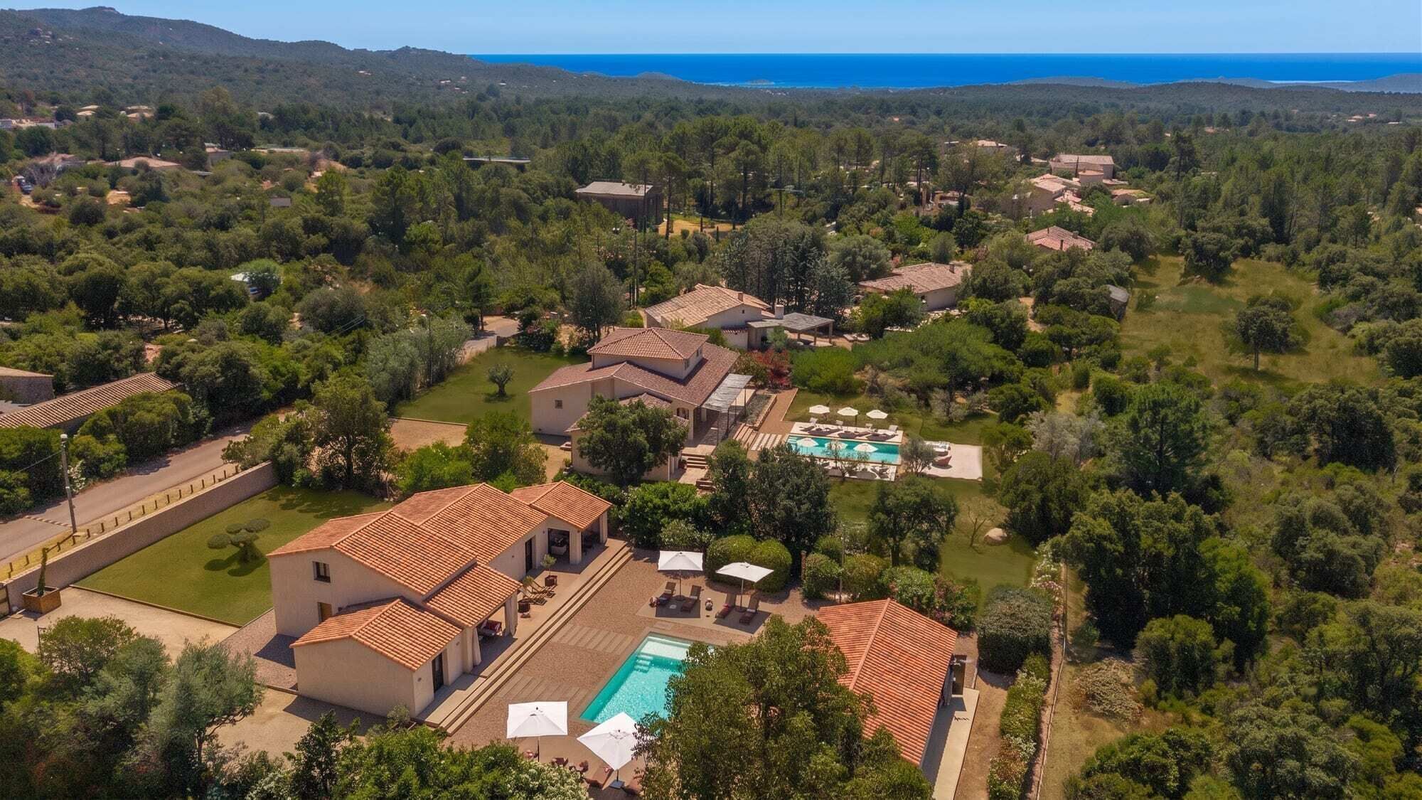 A residential area with multiple houses, a swimming pool, and a view of the sea.