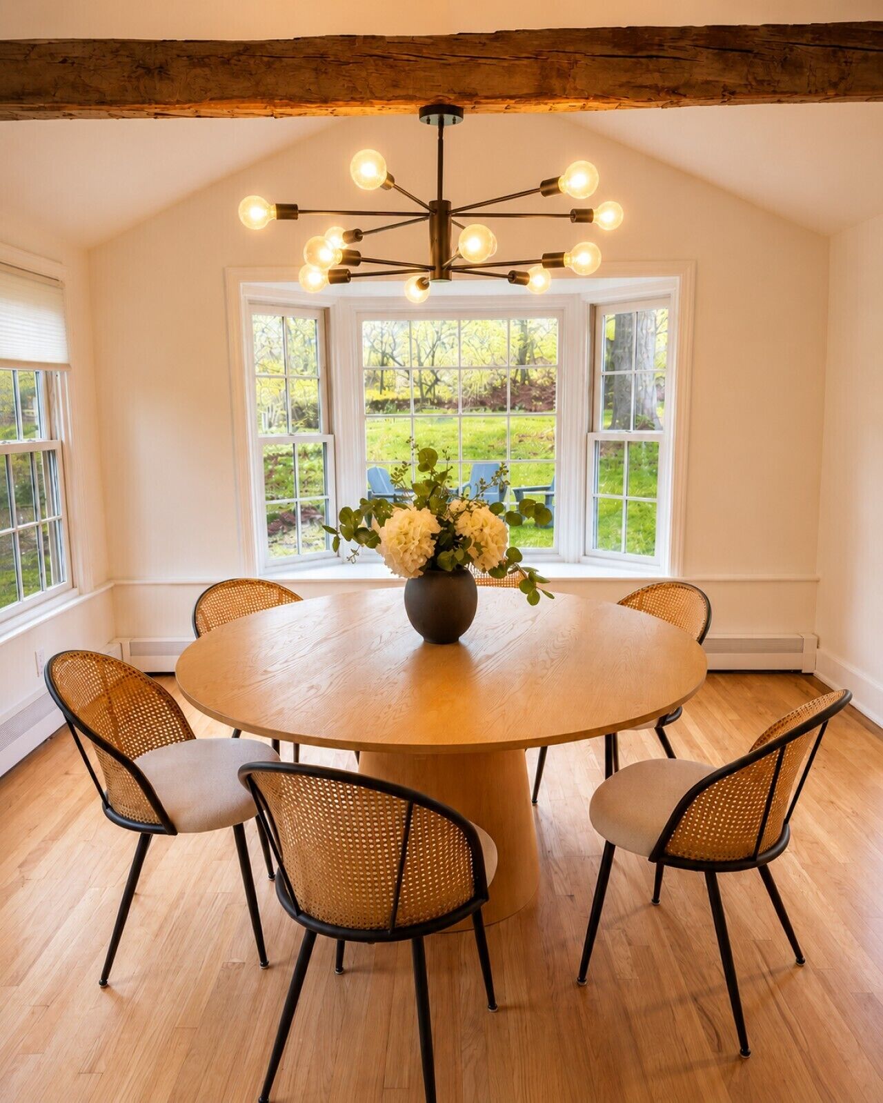 A round dining table with six chairs, a vase with flowers, and a modern chandelier.