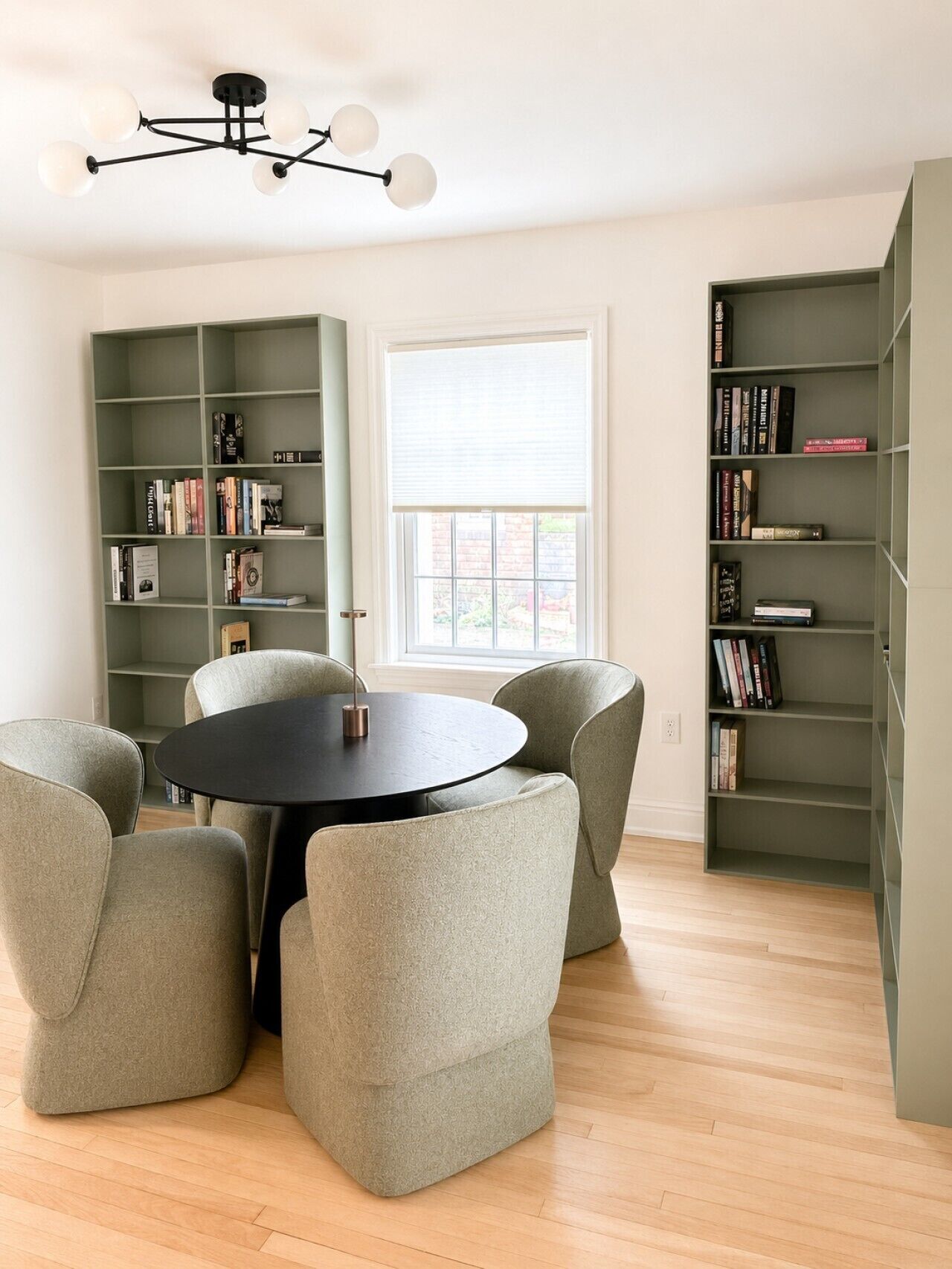 A room with a round table, four chairs, two bookshelves, and a ceiling light fixture.