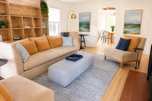 Ein modernes Wohnzimmer mit einer Couch, einem Hocker und einem Essbereich mit Stühlen und einem Tisch.