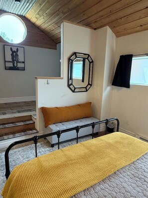 A bedroom with a bed, a sofa, a staircase, and a window.