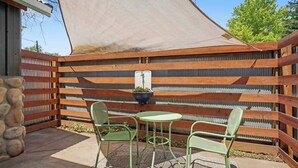 En terrasse med et bord og to stole, en hængende plantekasse og et stålhekkskjerm.