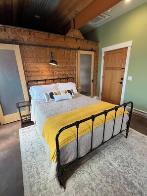 Un dormitorio con una cama, cabecera de madera, manta amarilla y mesita de noche.