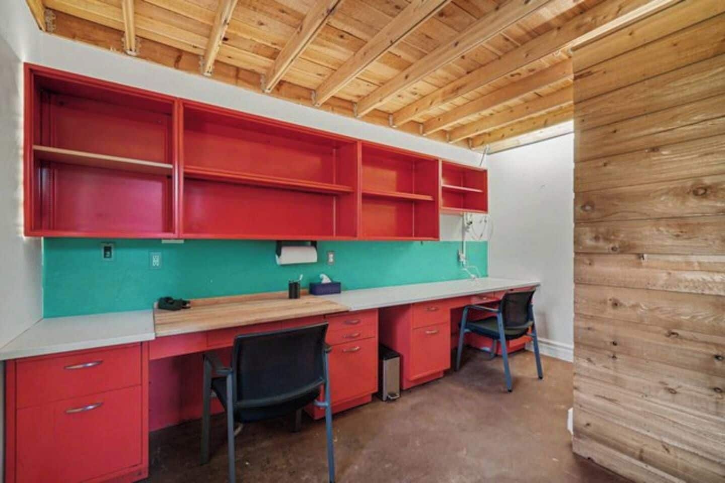 Cocina compacta con armarios rojos, salpicadero verde azulado y techo de madera.