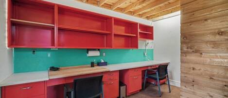 Cocina compacta con armarios rojos, salpicadero verde azulado y techo de madera.