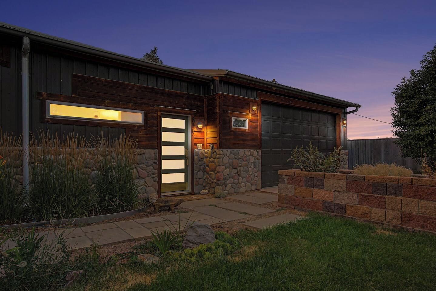 Une maison moderne avec un garage, des éléments décoratifs en pierre et une entrée bien éclairée.