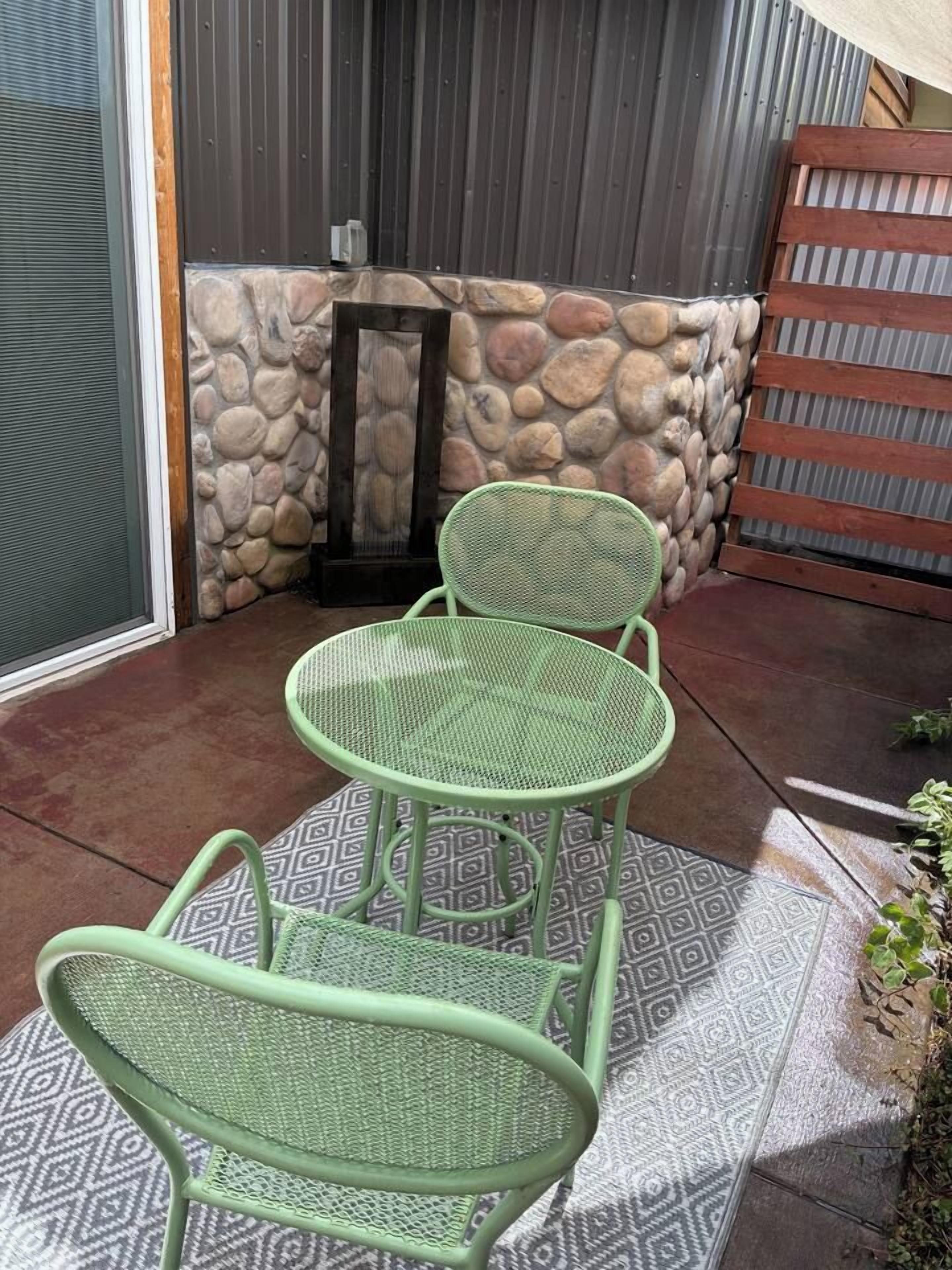 Un patio con un muro de piedra, una verja de metal y una mesa y sillas de metal verde.