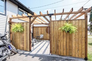 A wooden gate with a motorcycle parked to the left, a table and chairs in the background, and a hanging plant on the right.