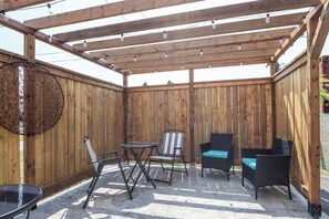 Una pérgola de madera con luces colgantes, una mesa redonda y dos sillas.