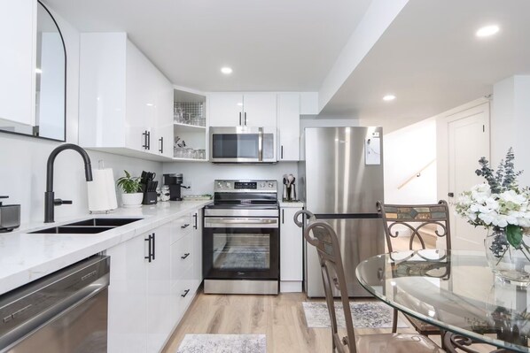 Una cocina moderna con armarios blancos, electrodomésticos de acero inoxidable, una mesa de comedor de vidrio y una planta decorativa.