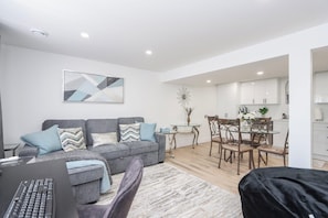 Una sala de estar moderna con un sofá gris, una mesa de comedor con sillas y una cocina al fondo.