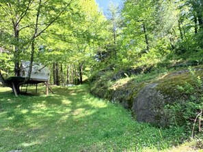 A campsite with a covered picnic table and a natural setting with trees and a grassy area. - The Woodland Retreat (Essex Junction)